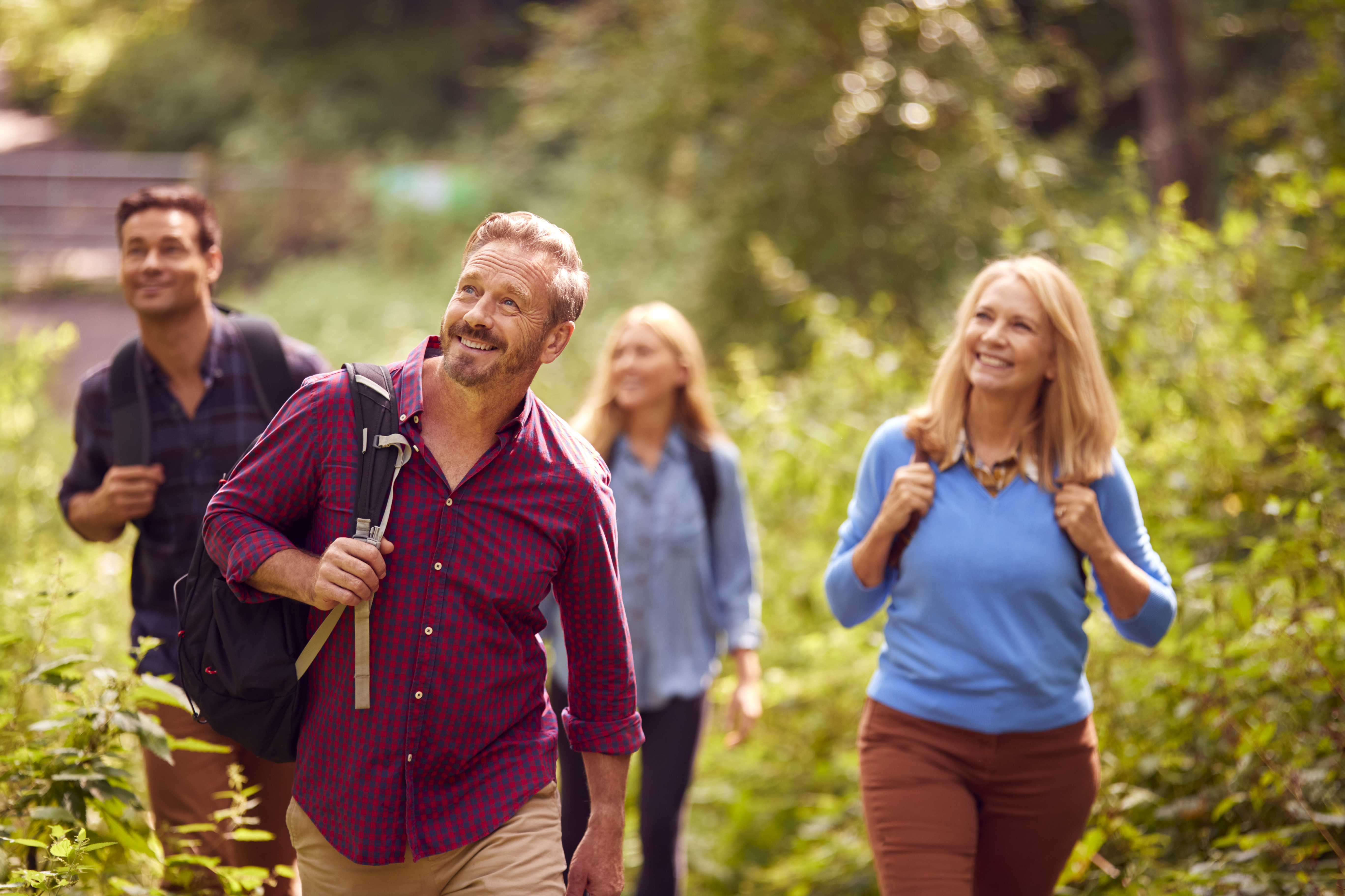 Mature And Mid Adult Couples In Countryside Hiking Along Path Through Forest Together